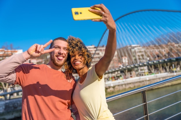 Photo multiracial couple through the city streets lifestyle selfie smiling by the river