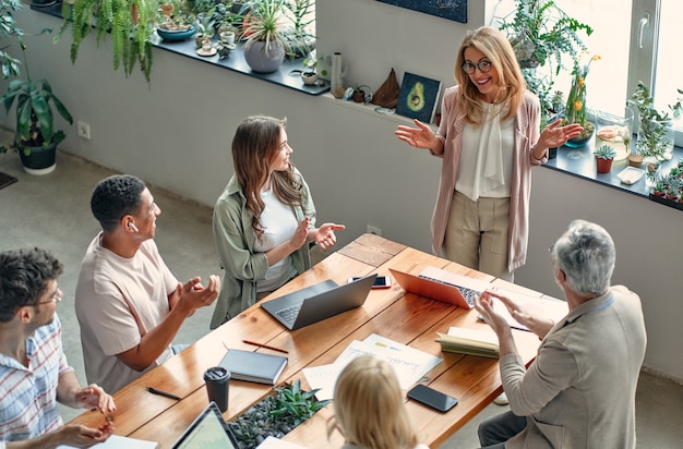 Multiracial creative people in modern office. Group of young business people and senior boss are working together with laptop, tablet, smart phone, notebook, graphs. Successful team in coworking