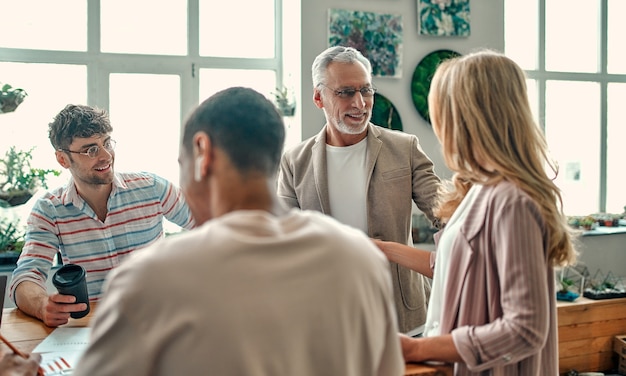 Multiracial creative people in modern office. Group of young business people and senior boss are working together with laptop, tablet, smart phone, notebook, graphs. Successful team in coworking