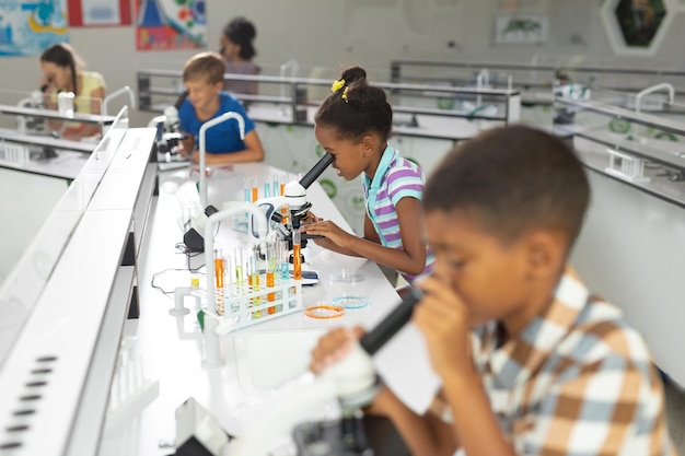 Photo multiracial elementary students using microscope during science practical in laboratory