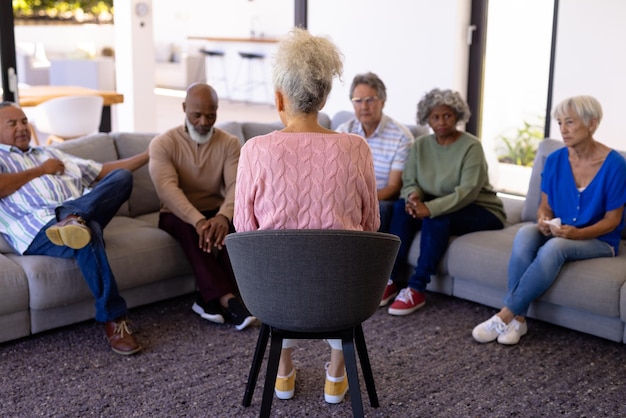 Multiracial female therapist talking with seniors sitting on sofa in group therapy at nursing home. Counseling, guidance, unaltered, psychotherapy, together, support, assisted living, retirement.