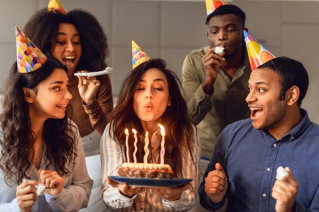 屋内でろうそくの火を吹き消す誕生日の女性を見ている多民族の友人