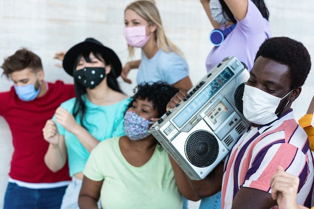 屋外でラジカセステレオで踊ったり音楽を聴いたりするマスクを持つ多民族の友達