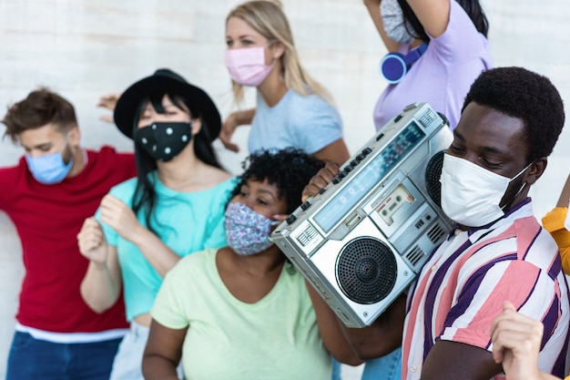 Photo multiracial friends with masks dancing and listening music with boombox stereo outdoors