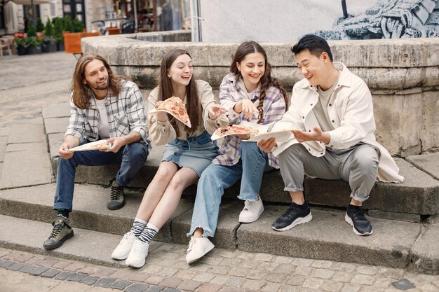 Multiracial group of friends eating a pizza on a street of old town