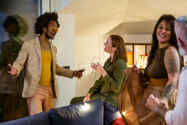 Multiracial group of friends having fun, dancing and socializing. Adult people tasting red wine talking and smiling during a private house party, celebration event for new year eve