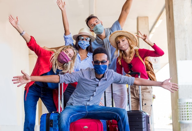 Multiracial group of friends at train station with luggage wearing protective mask