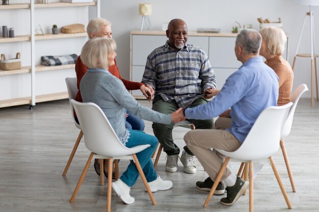 Photo multiracial group of happy pensioneers sitting in circle holding hands