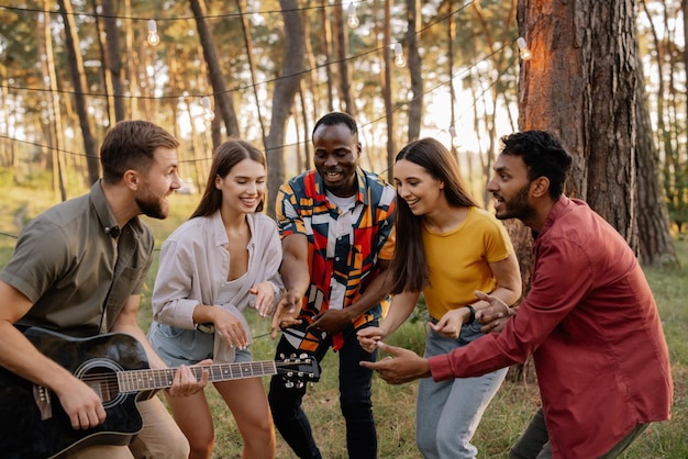 Многорасовая группа людей бородатый хипстер играет на гитаре и друзья танцуют и поют