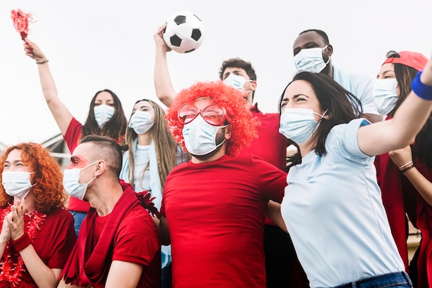 Gruppo multirazziale di appassionati di sport in maschera protettiva che urla allo stadio