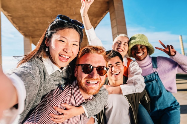 Multiracial group of young friends having fun make selfie photo with smartphone outdoors