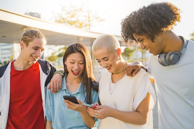 Amici adolescenti felici multirazziali che guardano il telefono e ridono nel campus