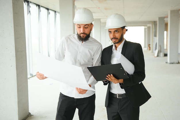 Multiracial male coworkers in hardhats discussing project on construction site