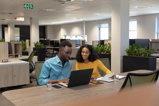 Multiracial male and female colleagues discussing over laptop sitting together at desk in workplace