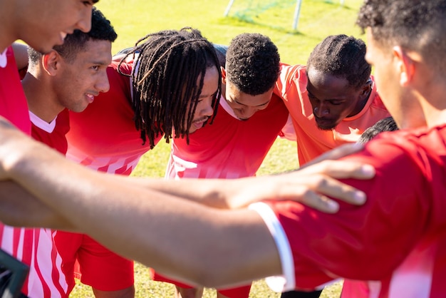 Multiracial male soccer players with arms around huddling and discussing in playground during match