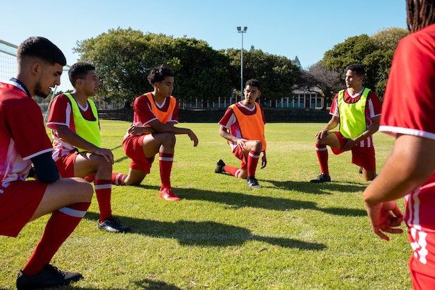 Multiracial male soccer team players stretching legs on grassy field in playground during summer