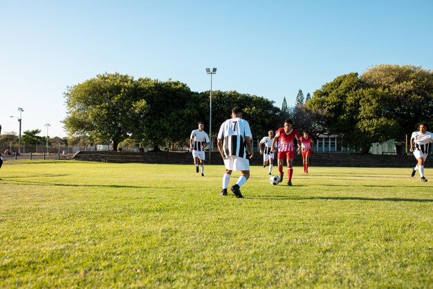 Photo multiracial male teams playing soccer match in playground against clear sky on sunny day, copy space