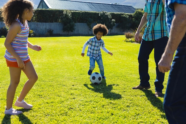 Photo multiracial multigeneration family playing soccer on grassy field in yard during sunny day