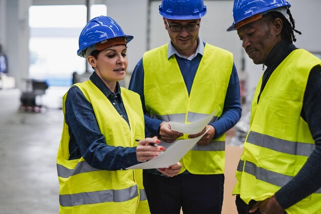 Multiracial people working inside robotic factory while wearing\
safety hardhat