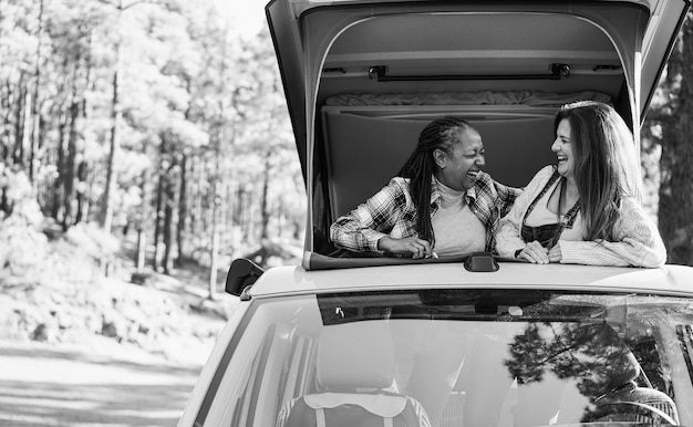 Multiracial senior women friends having fun inside camper van Focus on hands Black and white editing