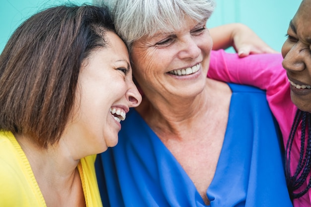 Donne anziane multirazziali che si divertono ad abbracciarsi all'aperto - focus sul volto femminile sinistro