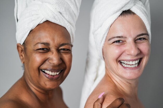 Multiracial senior women with diverse skin and body laughing together while wearing body towels - Main focus on right female face