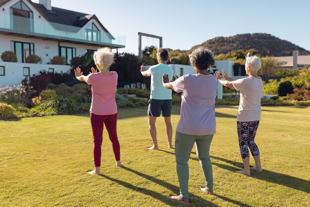 Foto anziani multirazziali che estendono le mani mentre stanno in piedi sul terreno erboso nel cortile di una casa di riposo