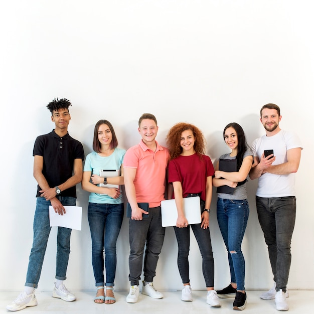 Foto gruppo di persone sorridente multirazziale che stanno davanti a fondo bianco che esamina macchina fotografica che tiene carta e dispositivo elettronico