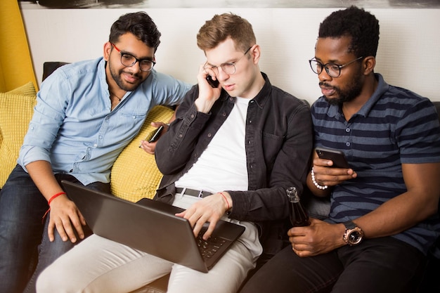 Multiracial young businesspeople discussing ideas for project, checking business plan on laptop together. Colleagues resting during the break, watching video online, talking on phone.