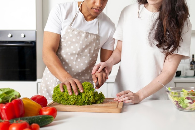 Многорасовая молодая пара готовит салат из овощей и зеленчука