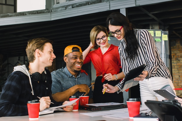 Giovani creativi multirazziali in ufficio moderno. gruppo di giovani imprenditori stanno lavorando insieme a laptop, tablet, smartphone, notebook. squadra hipster di successo nel coworking.