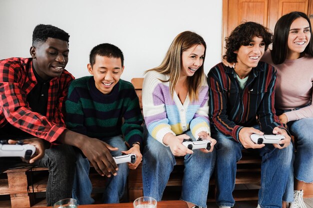 Photo multiracial young friends having fun playing video games at home - focus on center girl face