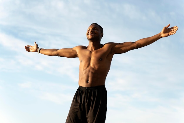 Multiracial young guy with his arms outstretched at the seaside standing next to the sea