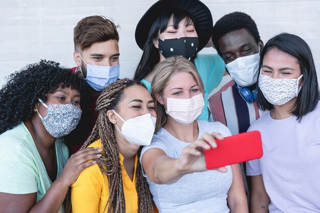 Multiracial young people taking selfie with phone camera while wearing protective masks