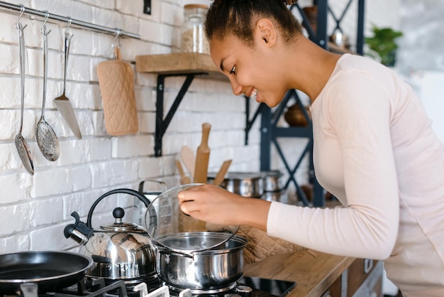 Multiracial young woman cooking in her cozy kitchen Side view of the smiling lady preparing lunch at home at the morning