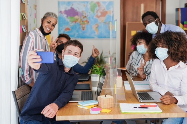 Multiraciale coworking-medewerkers die een selfie maken terwijl ze een veiligheidsmasker dragen voor de uitbraak van het coronavirus