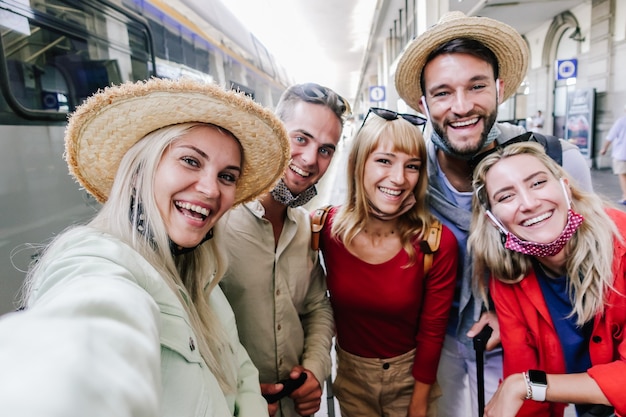 Multiraciale groep vrienden die een gezichtsmasker dragen en een selfie nemen op het treinstation. reizen, vakantie en vakantie nieuw normaal concept