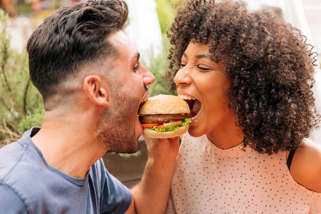 Multiraciale man en vrouw die samen smakelijke hamburger eten tijdens romantische date in restaurant in de zomer