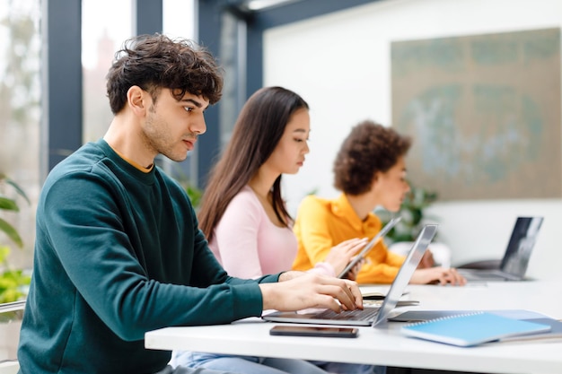 Multiraciale mannelijke en vrouwelijke studenten die studeren voor het maken van huiswerk met een op gadgets gerichte man