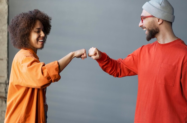 Foto multiraciale paar teamcollega's die een vuist bult delen die glimlachen terwijl ze over een grijze muurachtergrond staan