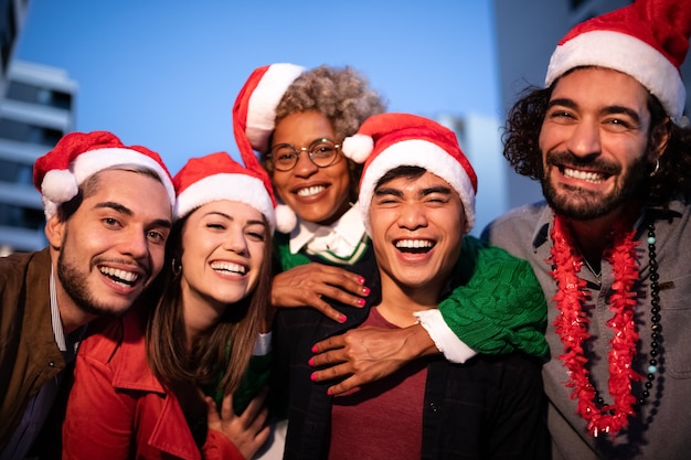 Multiraciale vrienden dragen kerstmutsen die naar de camera kijken en vieren samen Kerstmis Feestdagen