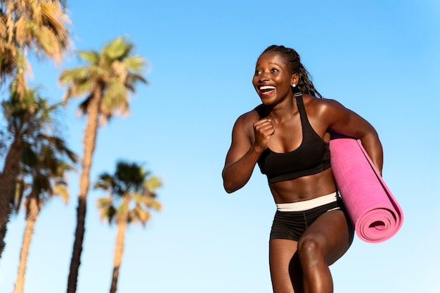 Multiraciale vrouw met roze yogamat terwijl ze op het strand rent