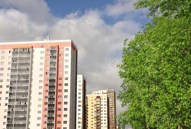 multistorey new houses in a row green foliage of trees blue sky with white clouds without man