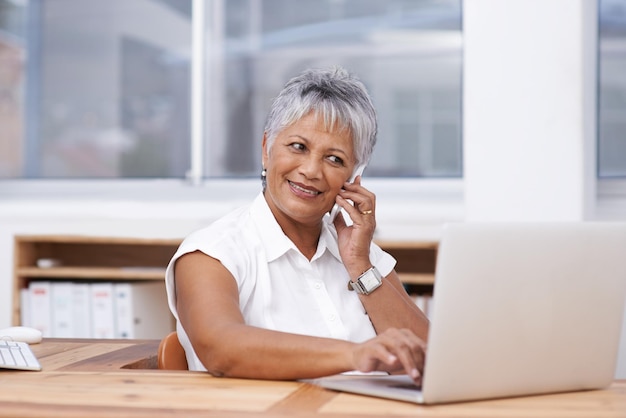 Multitasken als een pro Shot van een volwassen zakenvrouw die telefoneert terwijl ze een laptop gebruikt