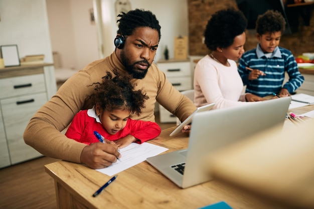 Multitasking black father working at home while daughter is sitting on his lap