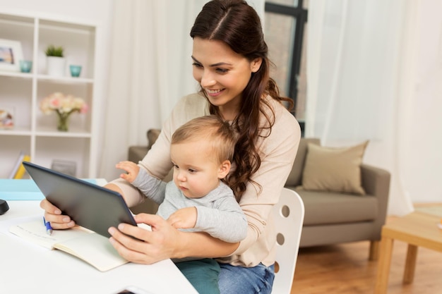 Multitasking education motherhood and technology concept happy mother student with baby and tablet pc computer learning at home