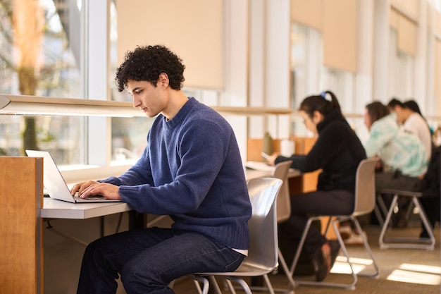 Multitasking overworked serious Latin American student online studying in a modern library campus