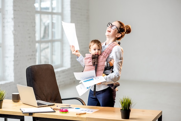 Multitasking zakenvrouw met een stapel papieren documenten met haar zoontje op kantoor