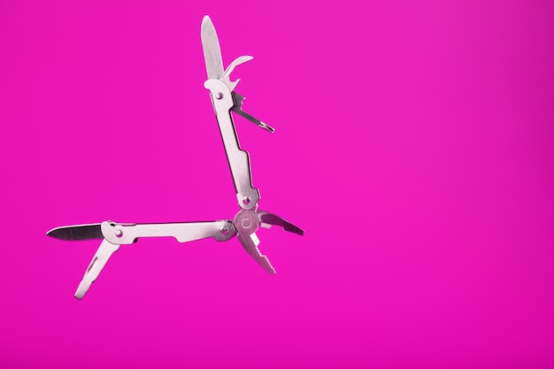 Multitool is a multi-functional tool on a pink background. The concept of an open, flying multi-tool with free space.