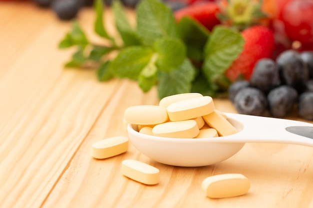 Photo multivitamin and mutimineral capsuls nutritional supplement in spoon on wooden table with variety fruit